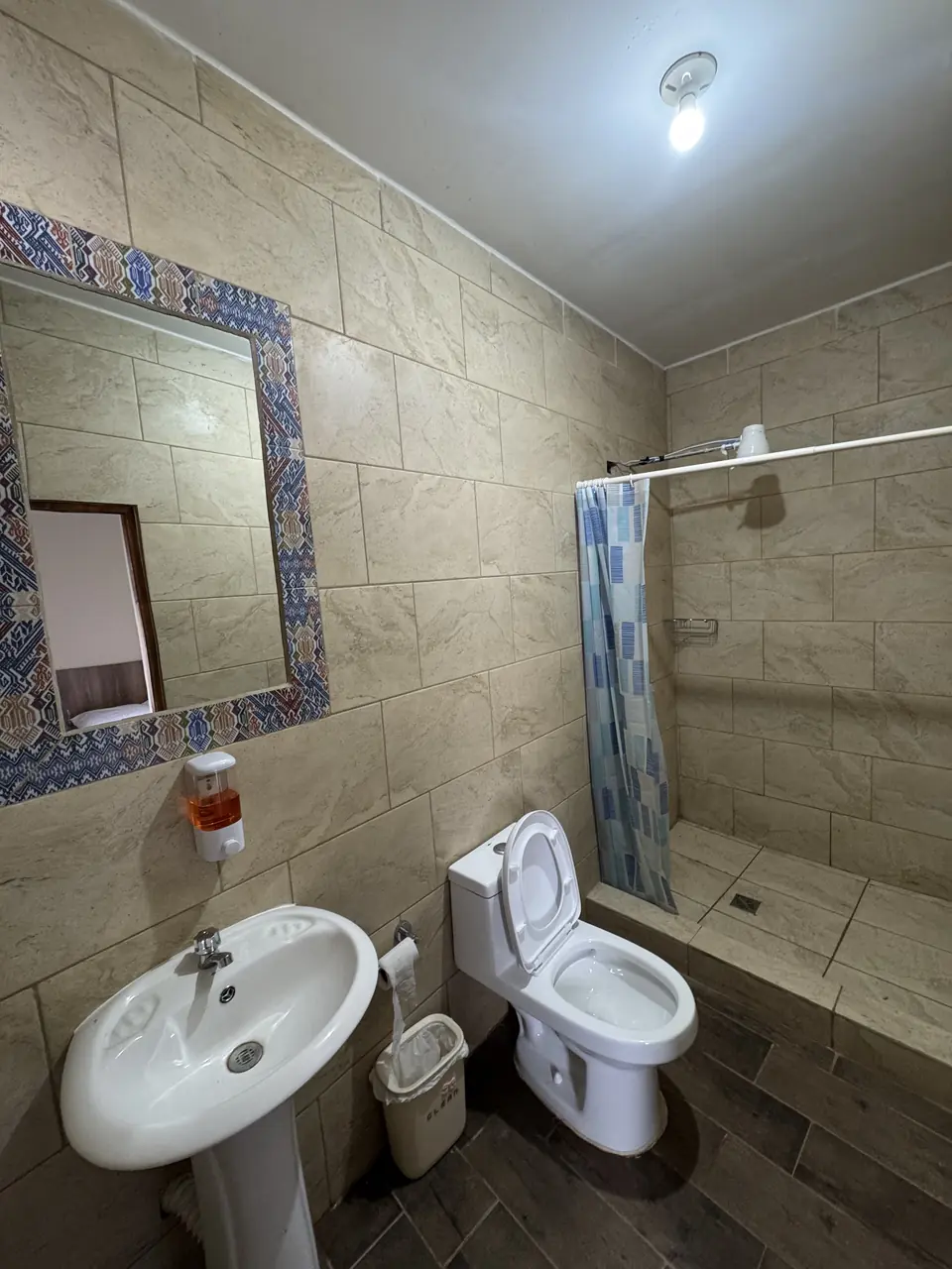 Baño privado con ducha, lavamanos y espejo con marco de azulejo